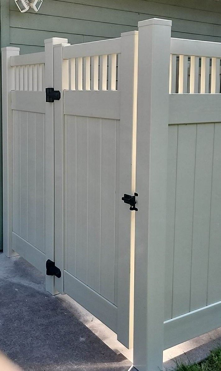 A white vinyl fence with a black gate is in front of a house.