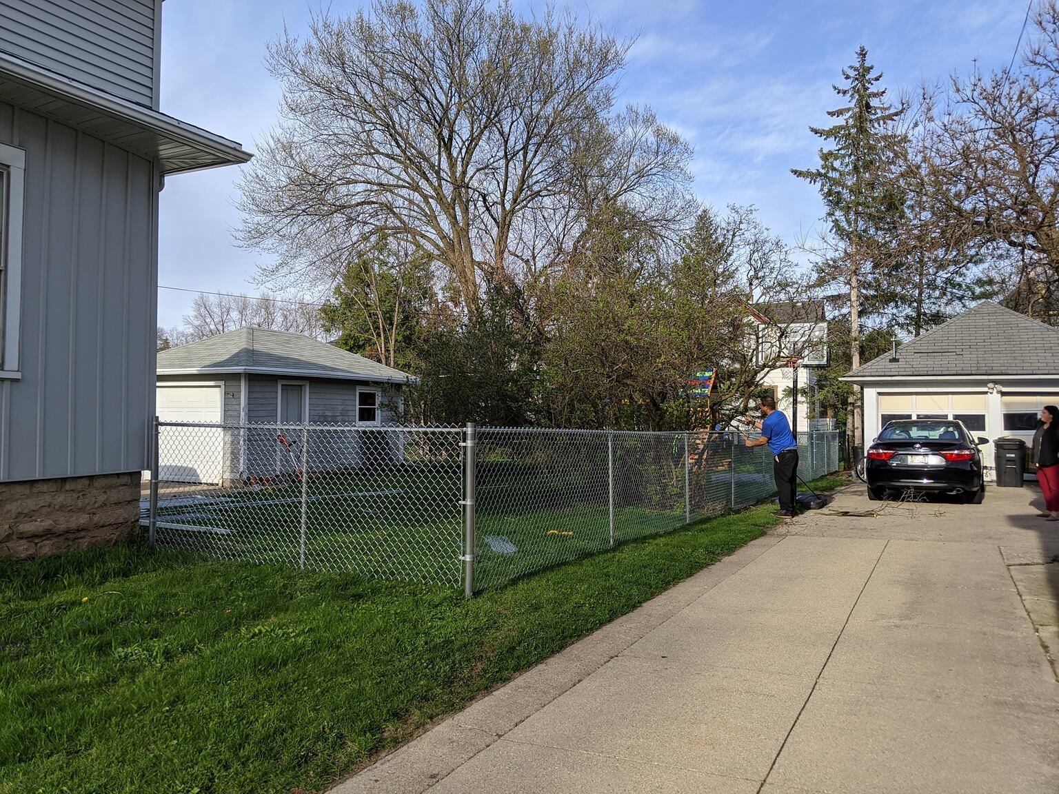 A man is standing next to a chain link fence in front of a house.