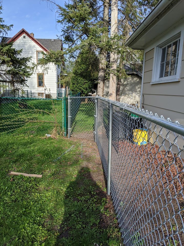 A chain link fence is surrounding a yard next to a house.