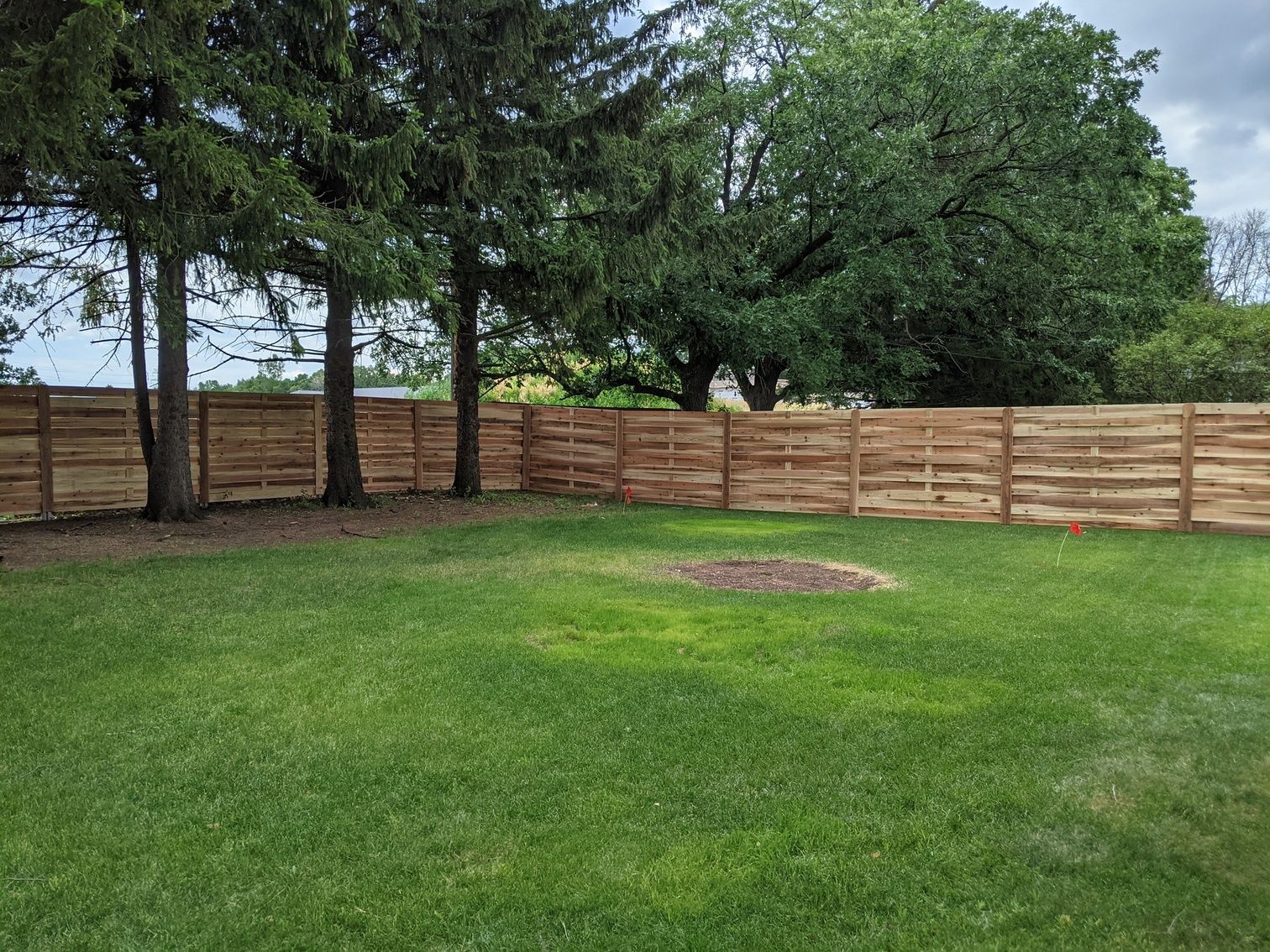 A wooden fence surrounds a large lush green yard.