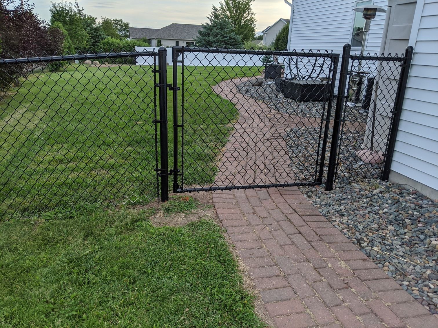 A chain link fence surrounds a brick walkway leading to a house.