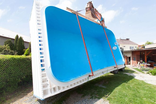 Large blue swimming pool being loaded onto a truck in a suburban yard