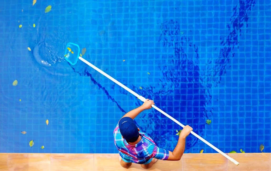 Person cleaning a blue tiled pool with a long pole, viewed from above