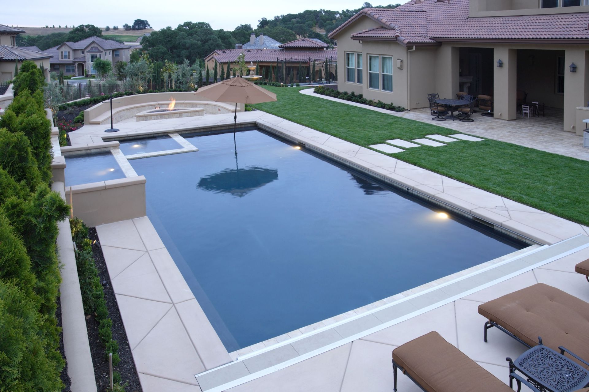 Backyard with a rectangular pool, patio seating, and a modern house at sunset