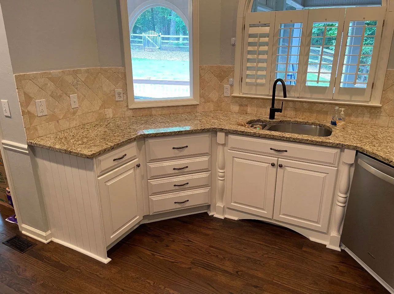 A kitchen with white cabinets , granite counter tops , a sink and a window.
