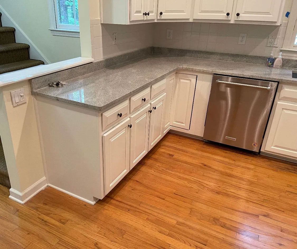 A kitchen with white cabinets , granite counter tops , and a stainless steel dishwasher.