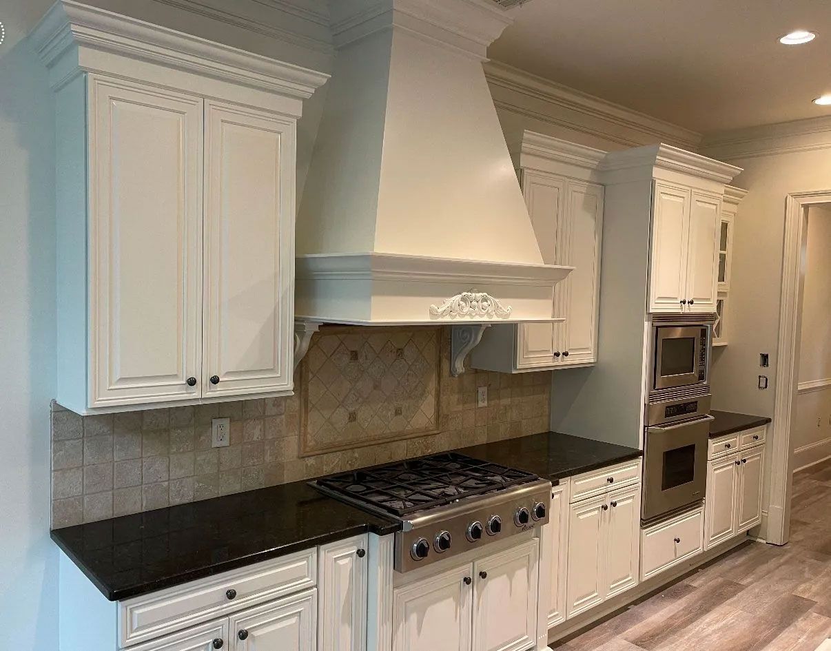 A kitchen with white cabinets , black counter tops , a stove , and a hood.