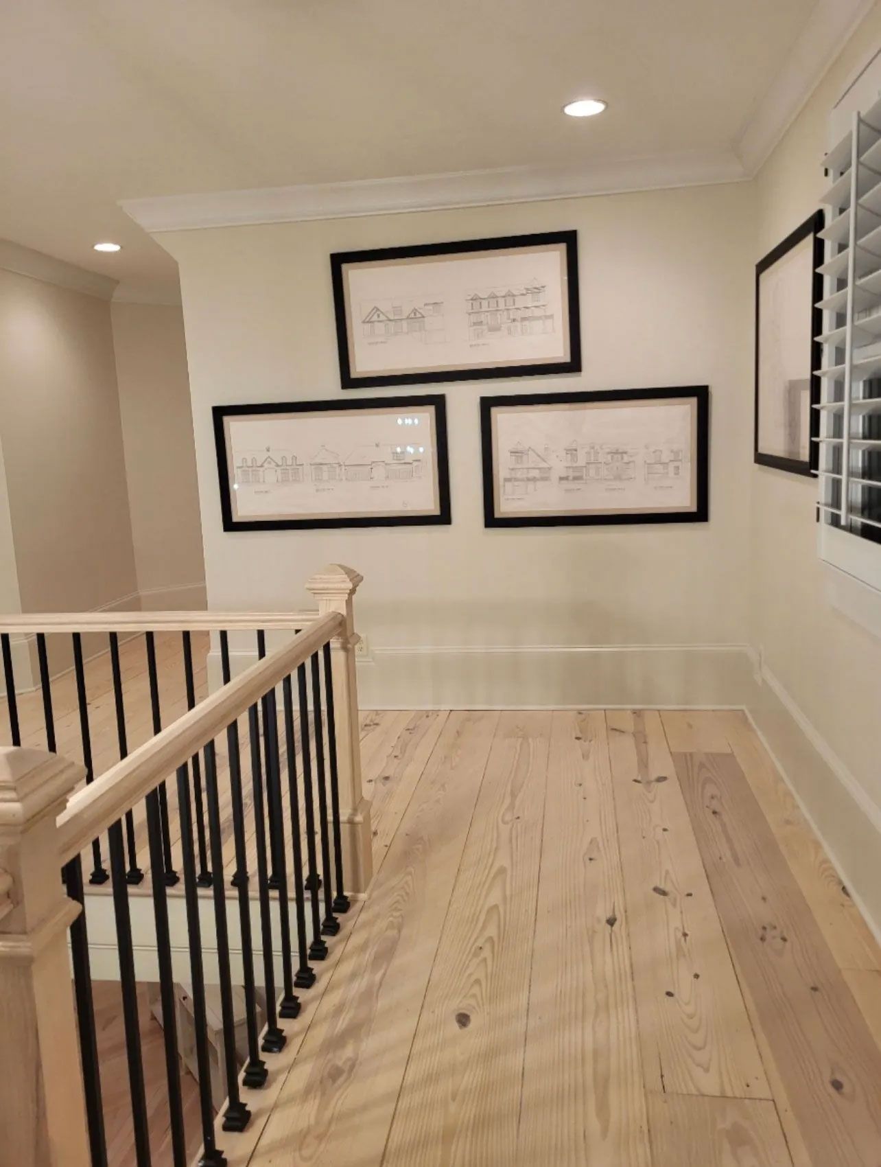 A hallway with a railing and three framed pictures on the wall.