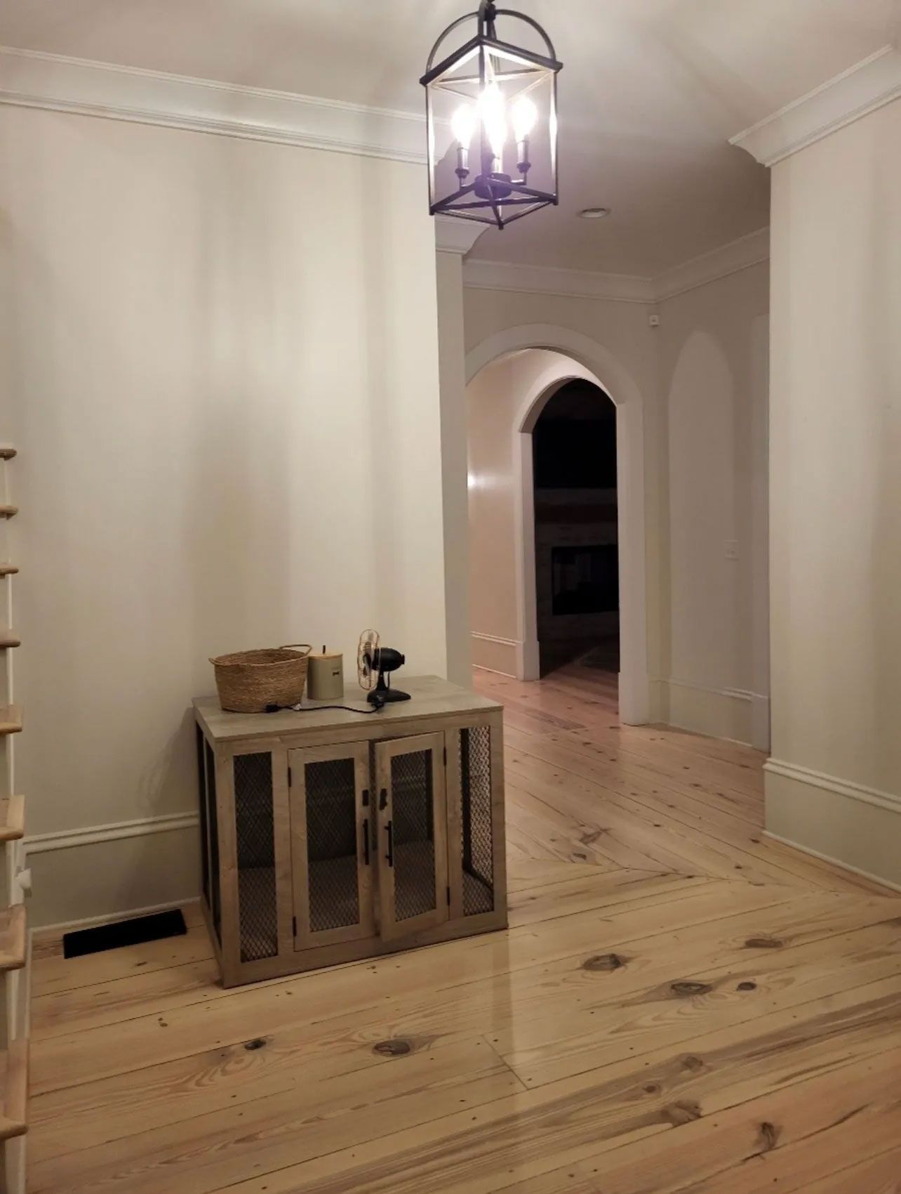 A hallway with hardwood floors and a dog kennel in the middle.