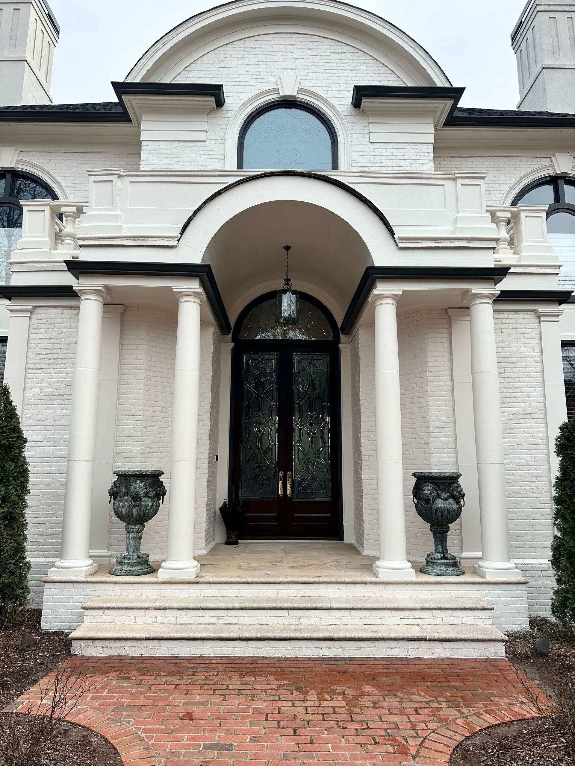 The front of a white brick house with columns and a black door.