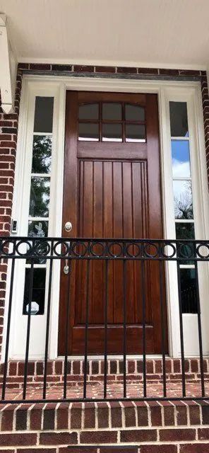 The front door of a brick house with a wooden door and a wrought iron railing.