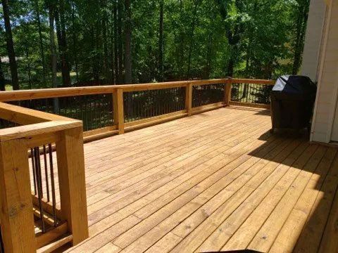 A large wooden deck with a grill and trees in the background.