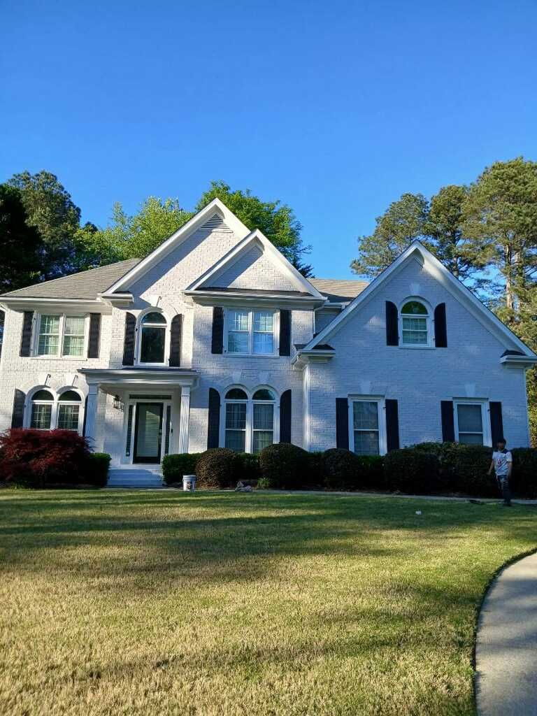 A white house with a black roof is surrounded by trees.