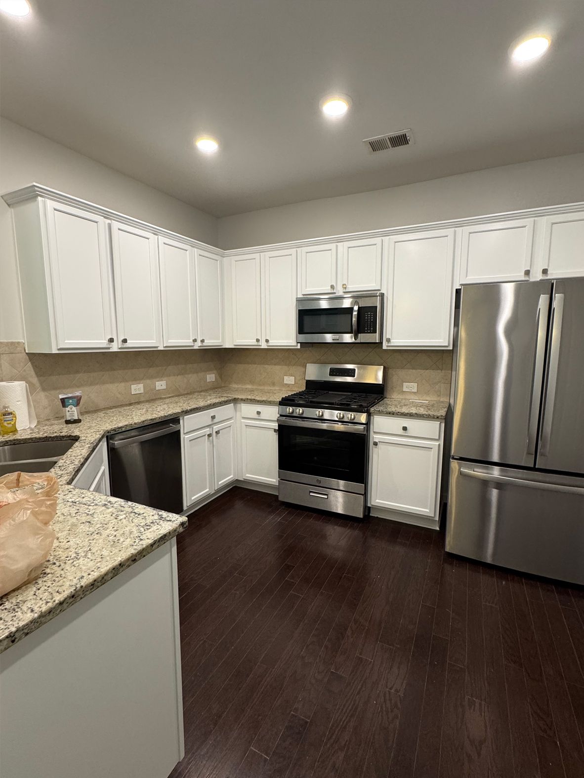 White kitchen with stainless steel appliances and dark wood floors.