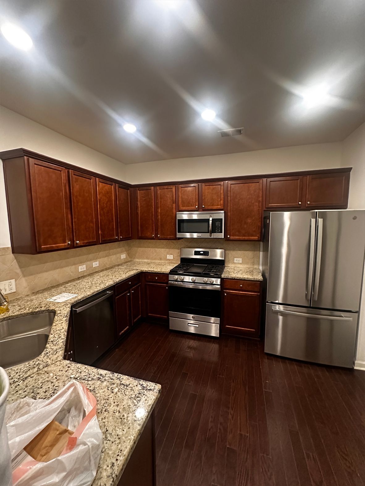 L-shaped kitchen with dark wood cabinets, stainless steel appliances, granite countertops, and dark wood flooring.