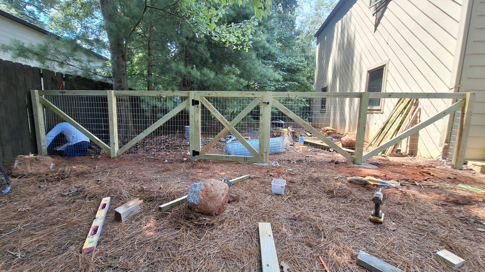 Workers building a wooden fence in a backyard with mulch.