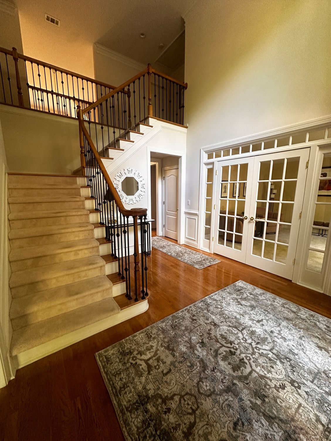 A two-story foyer with a staircase, hardwood floors, a rug, and double doors.