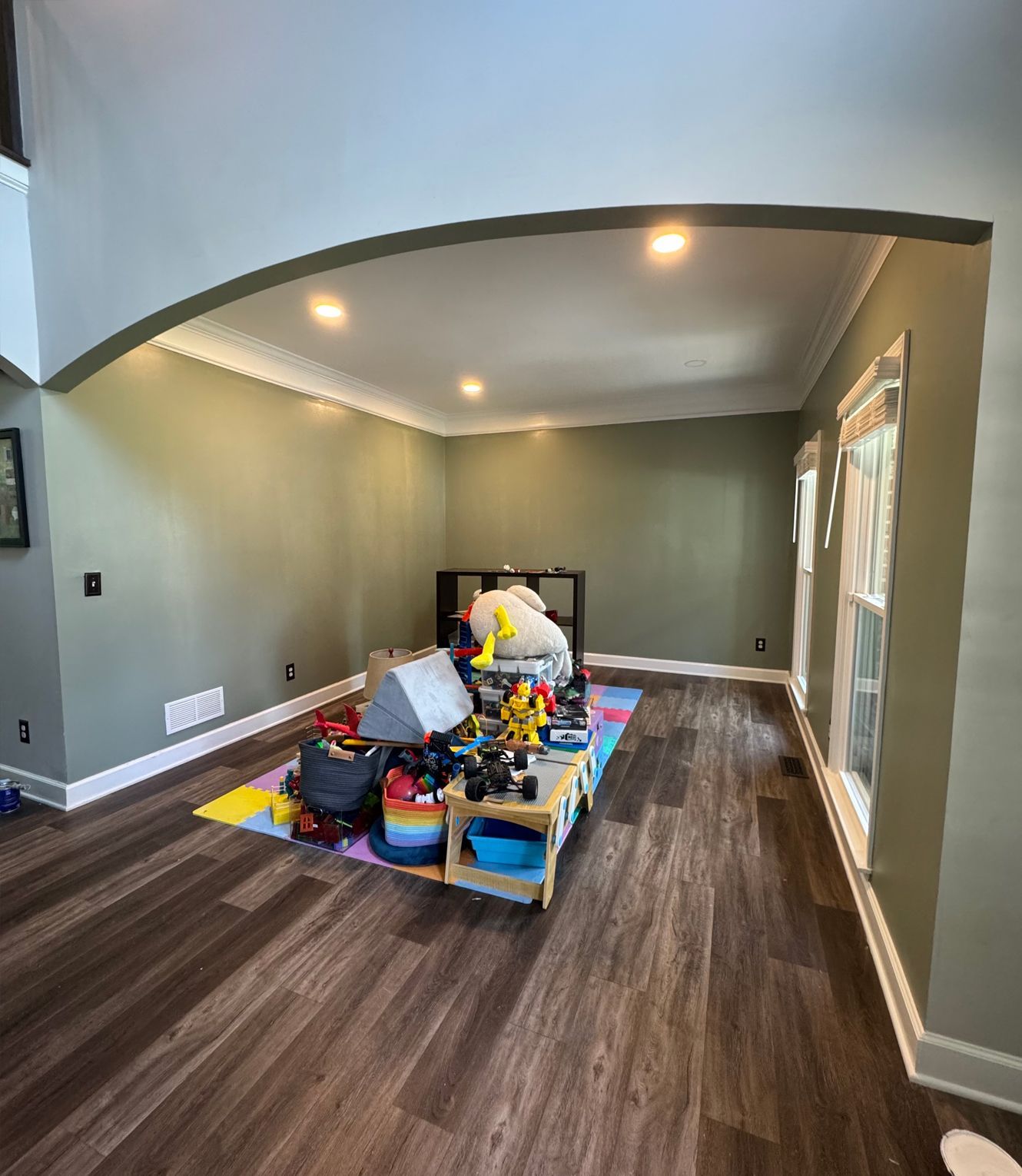 A room with toys on a colorful mat, green walls, wood floors, and an arched ceiling.