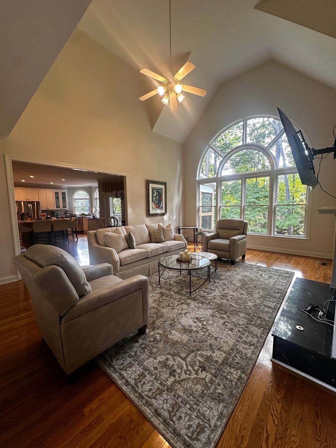 Living room with beige sofas, rug, large window, hardwood floors, and high ceilings.