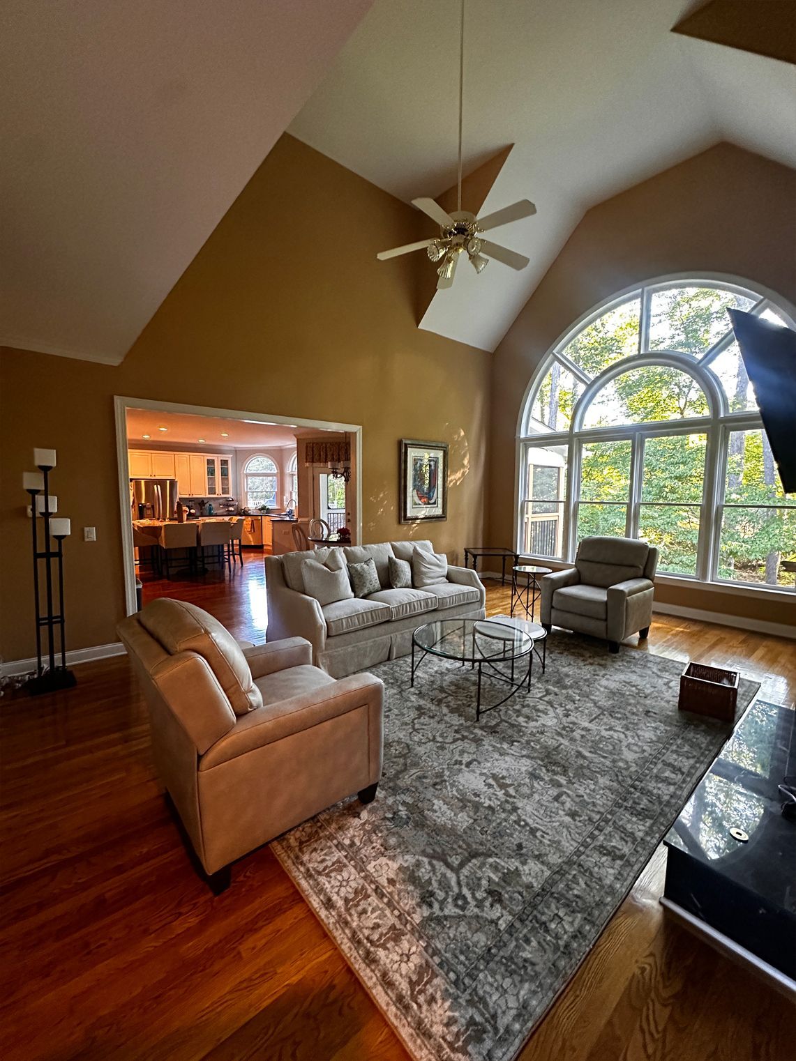 Living room with tan walls, arched window, and light-colored furniture on a patterned rug.