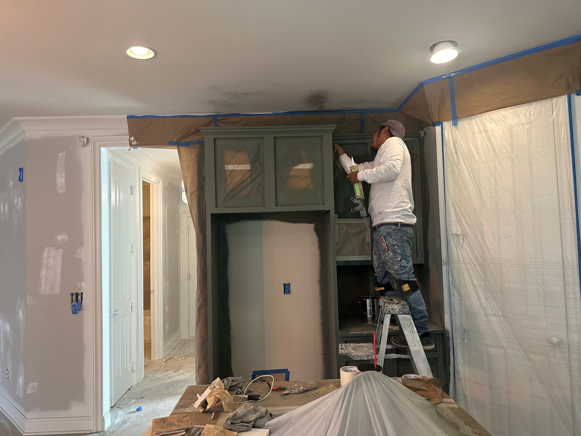 A man is standing on a ladder painting a cabinet in a room.