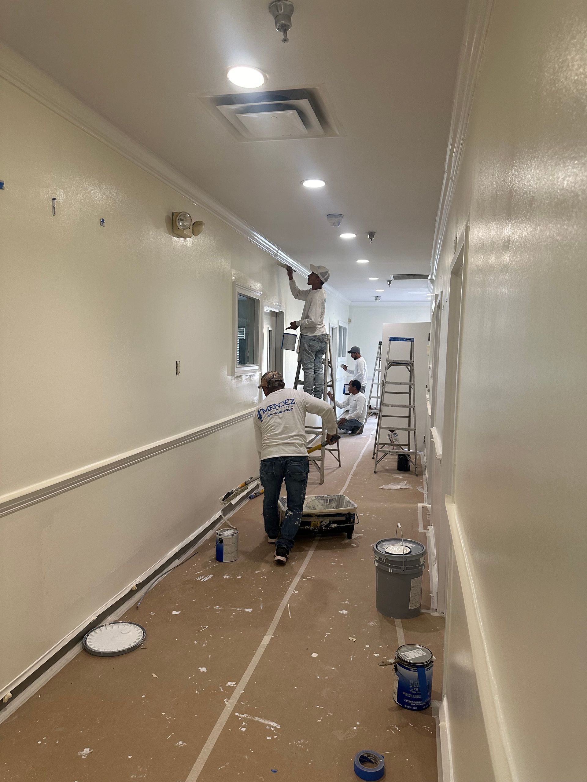 A group of people are painting a hallway in a building.