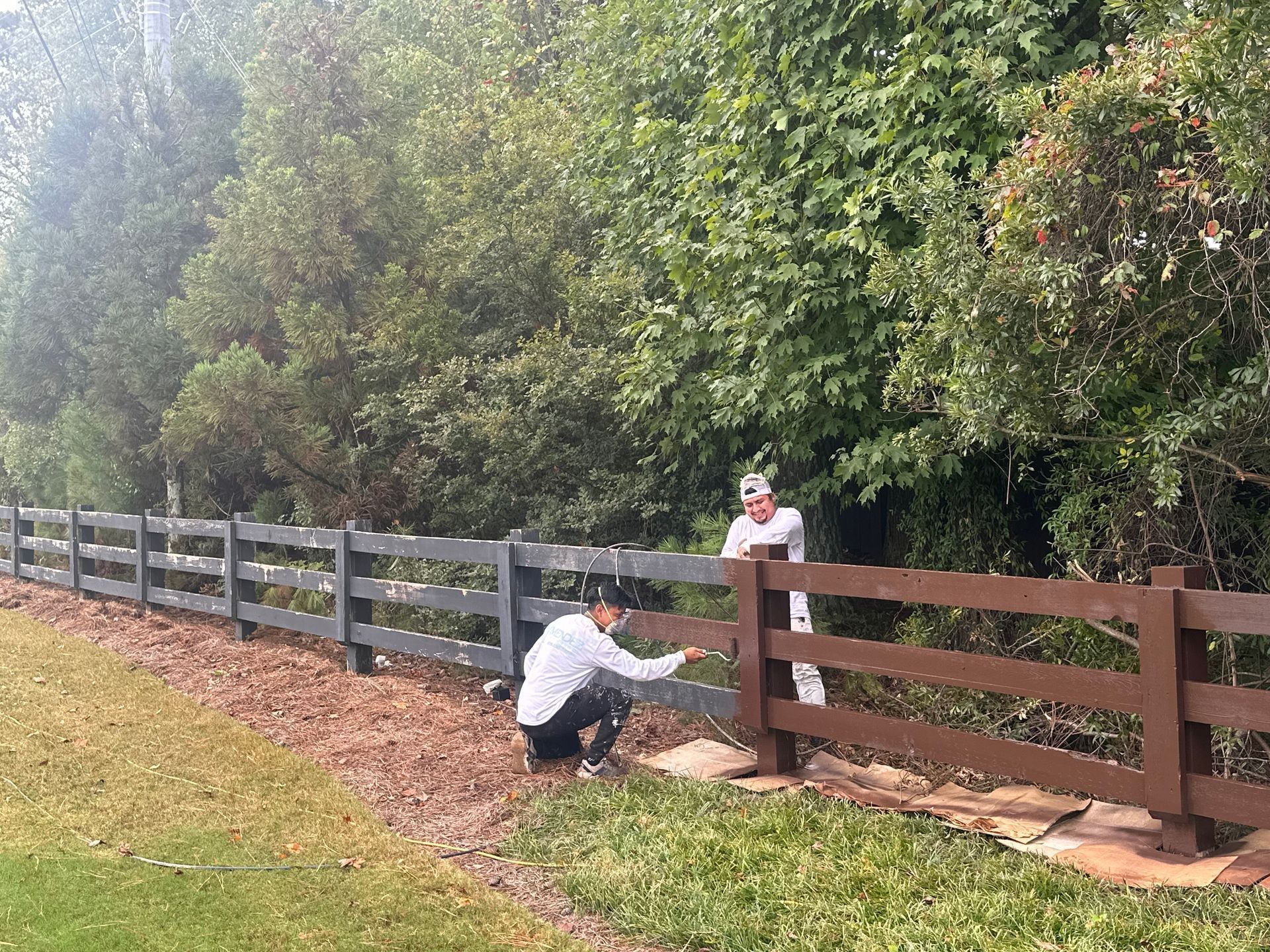 A man is kneeling down next to a wooden fence.