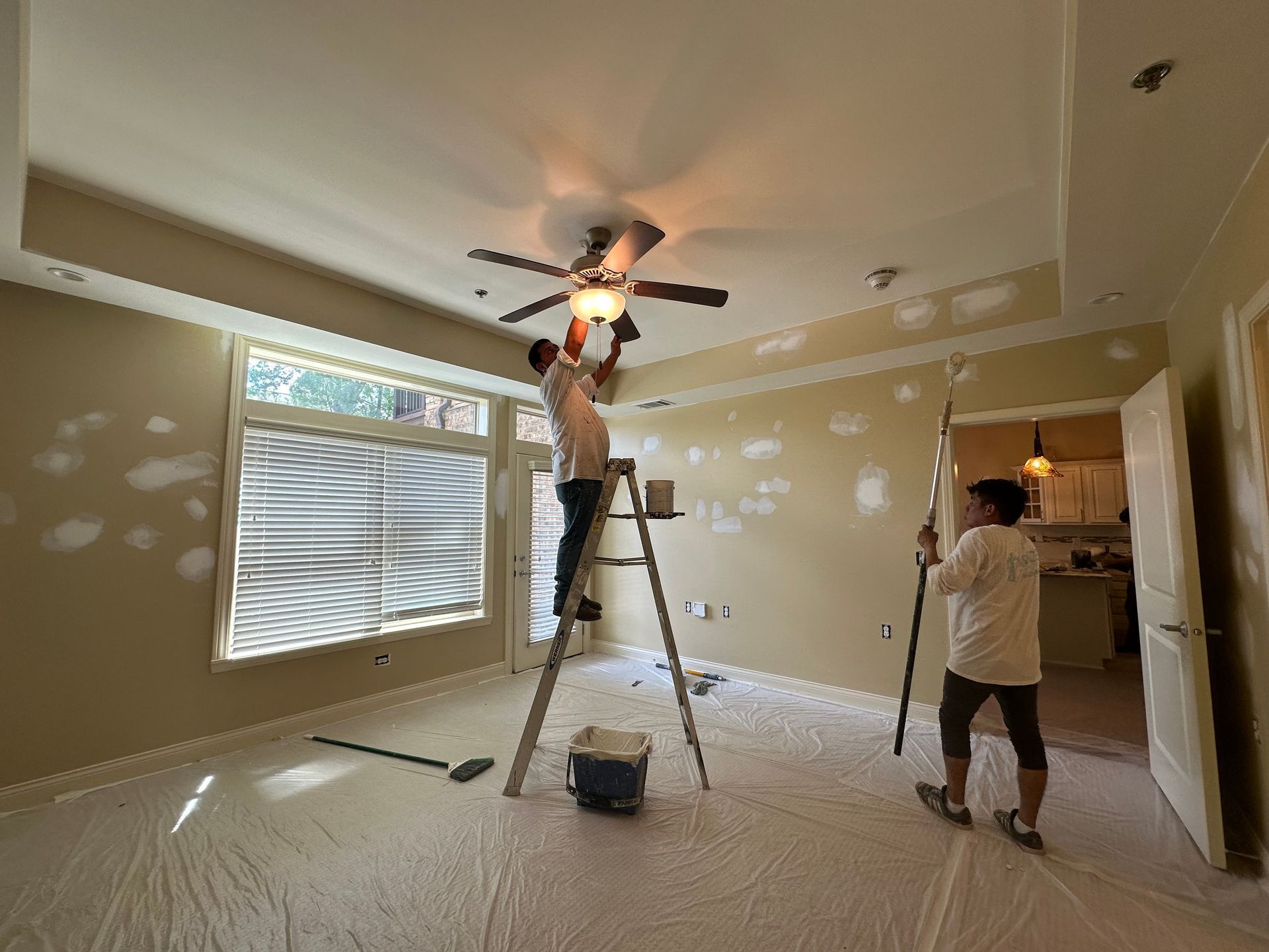 Two men are painting a ceiling fan in a room.