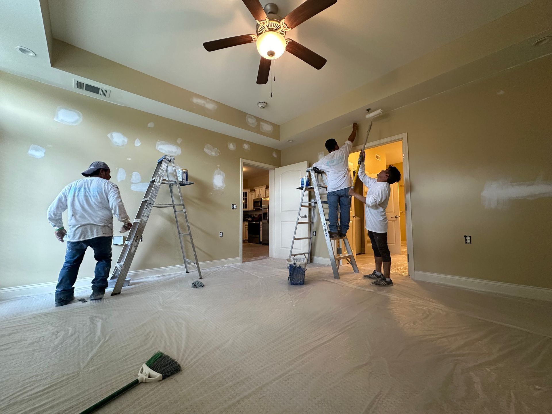 A group of people are painting a room with a ceiling fan.