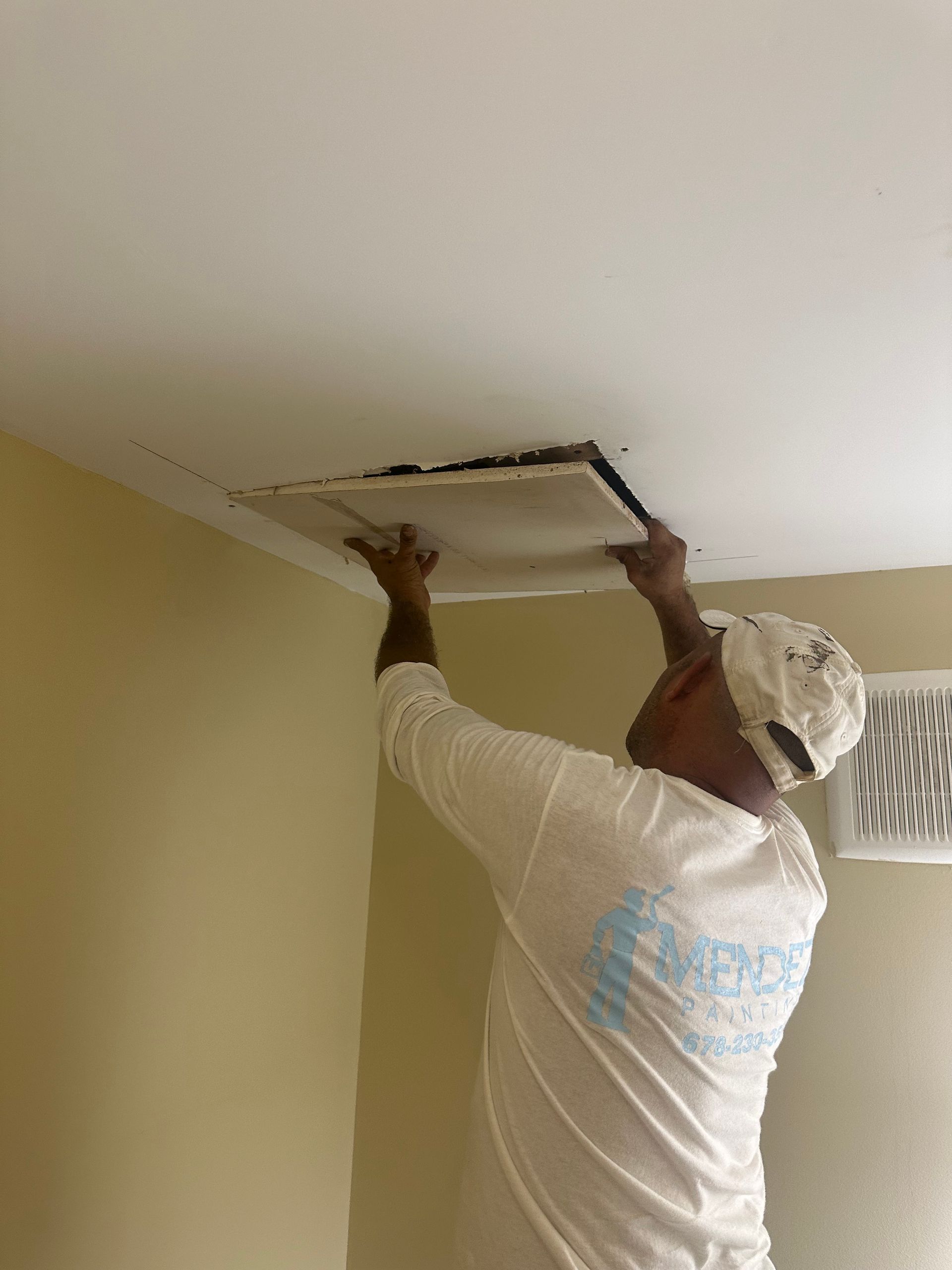 A man in a white shirt is fixing a hole in the ceiling.