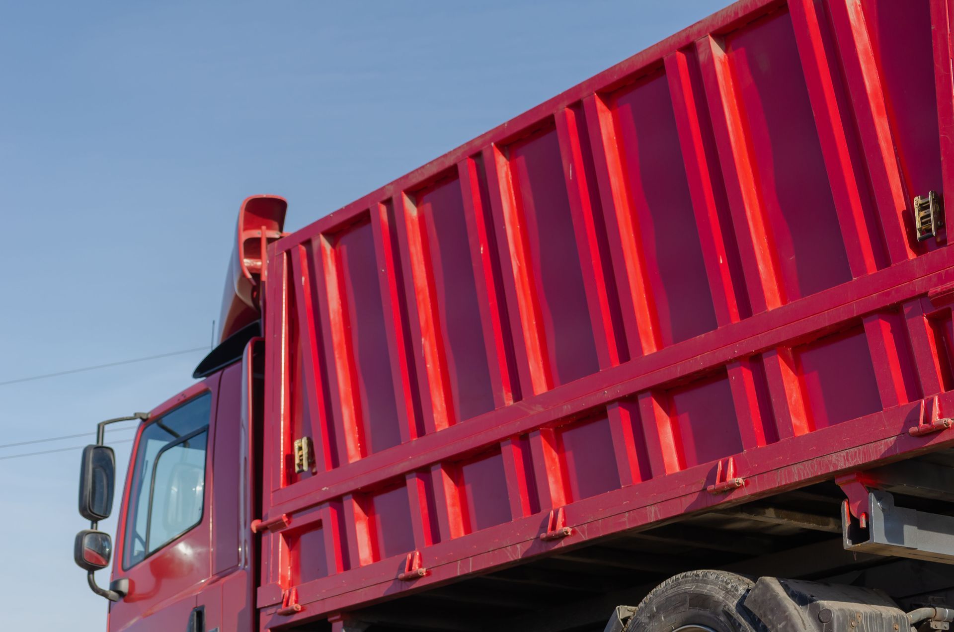 Red dump truck bed and cab against a blue sky.