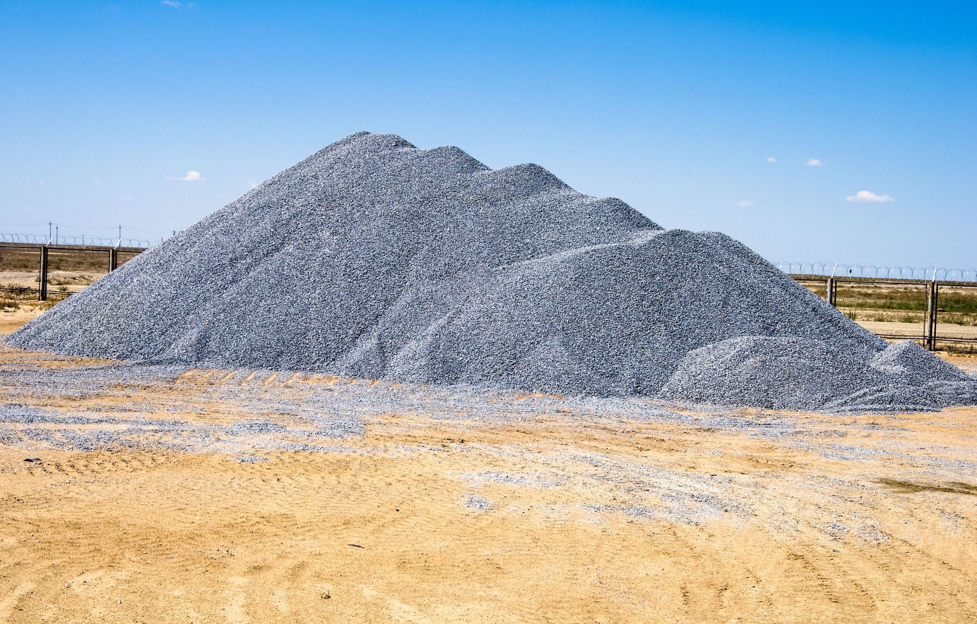 Large pile of gray gravel on tan dirt, under a blue sky.