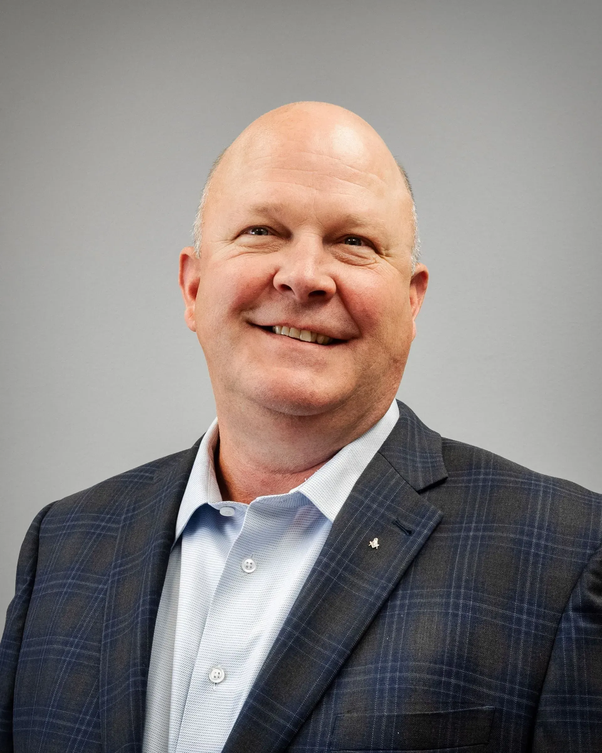 Smiling man in a dark blazer and light blue shirt against a gray background