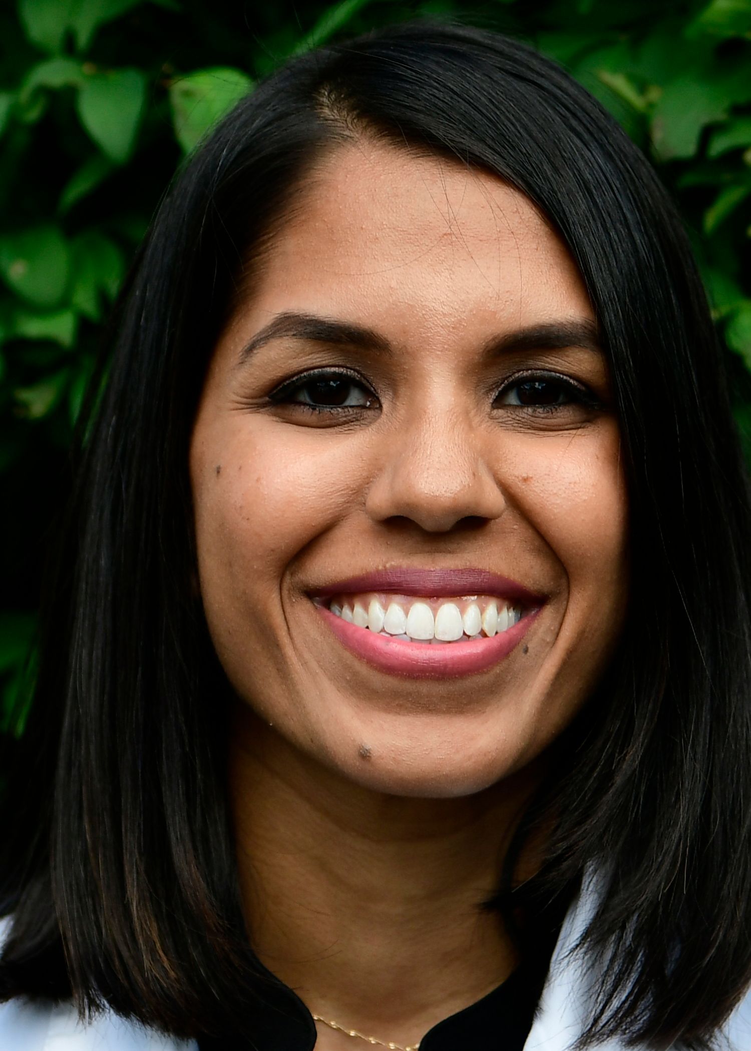 Woman with dark hair smiles at the camera, against a blurred green background.