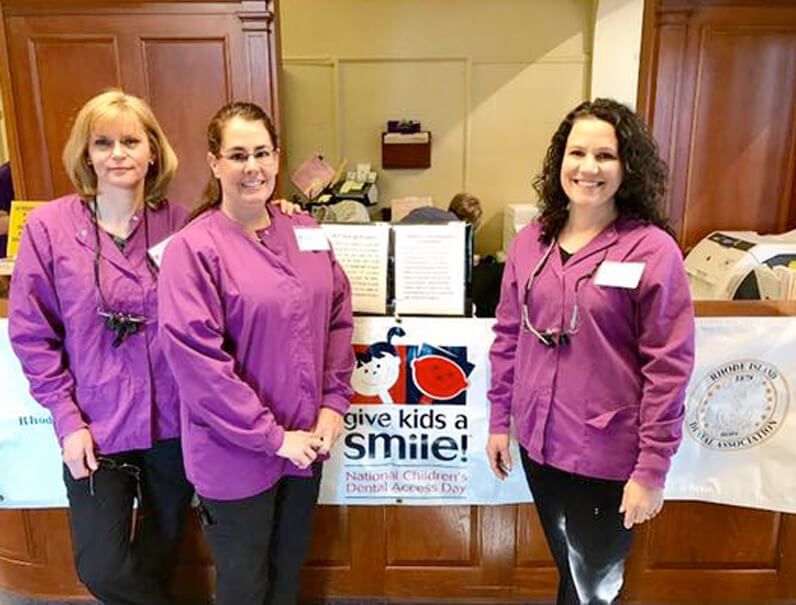 Three people in purple uniforms stand smiling in front of a 