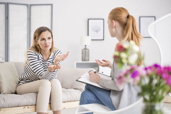 Woman talking with therapist in a bright living room, seated on a sofa during a counseling session