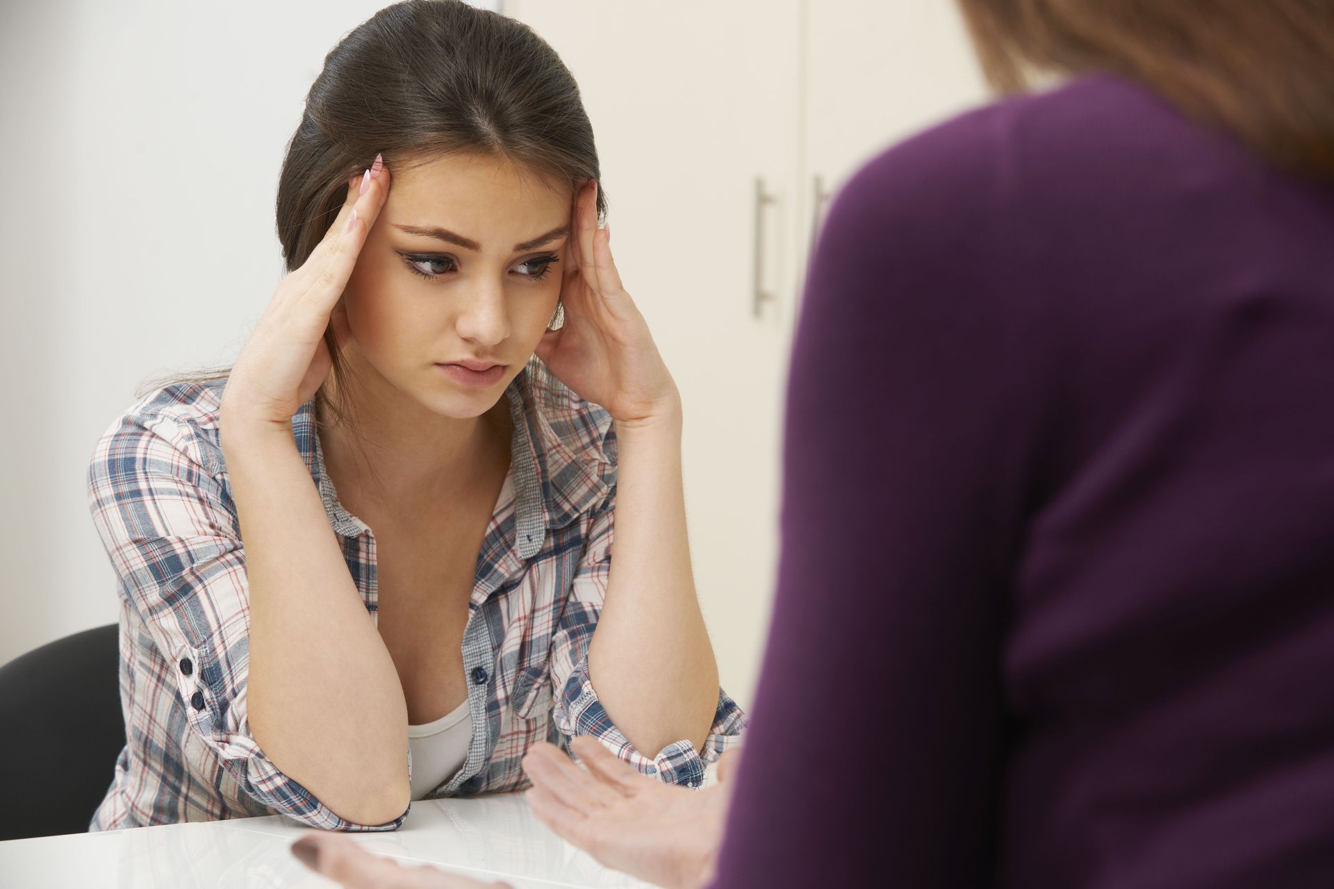 Woman sitting at a table with hands on her temples, looking stressed during a conversation