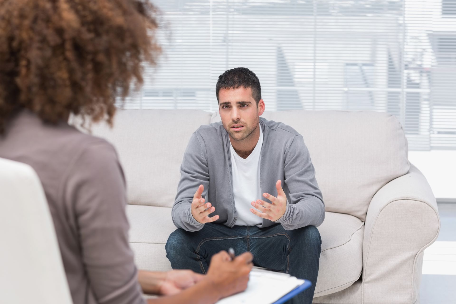 Man speaking during a counseling session on a white couch, with a clipboard in the foreground