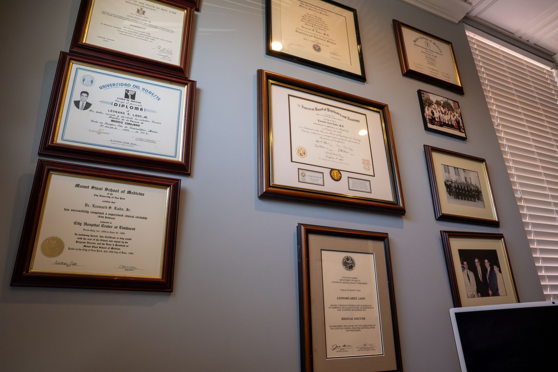 Wall of framed certificates and awards on a light blue wall beside a window
