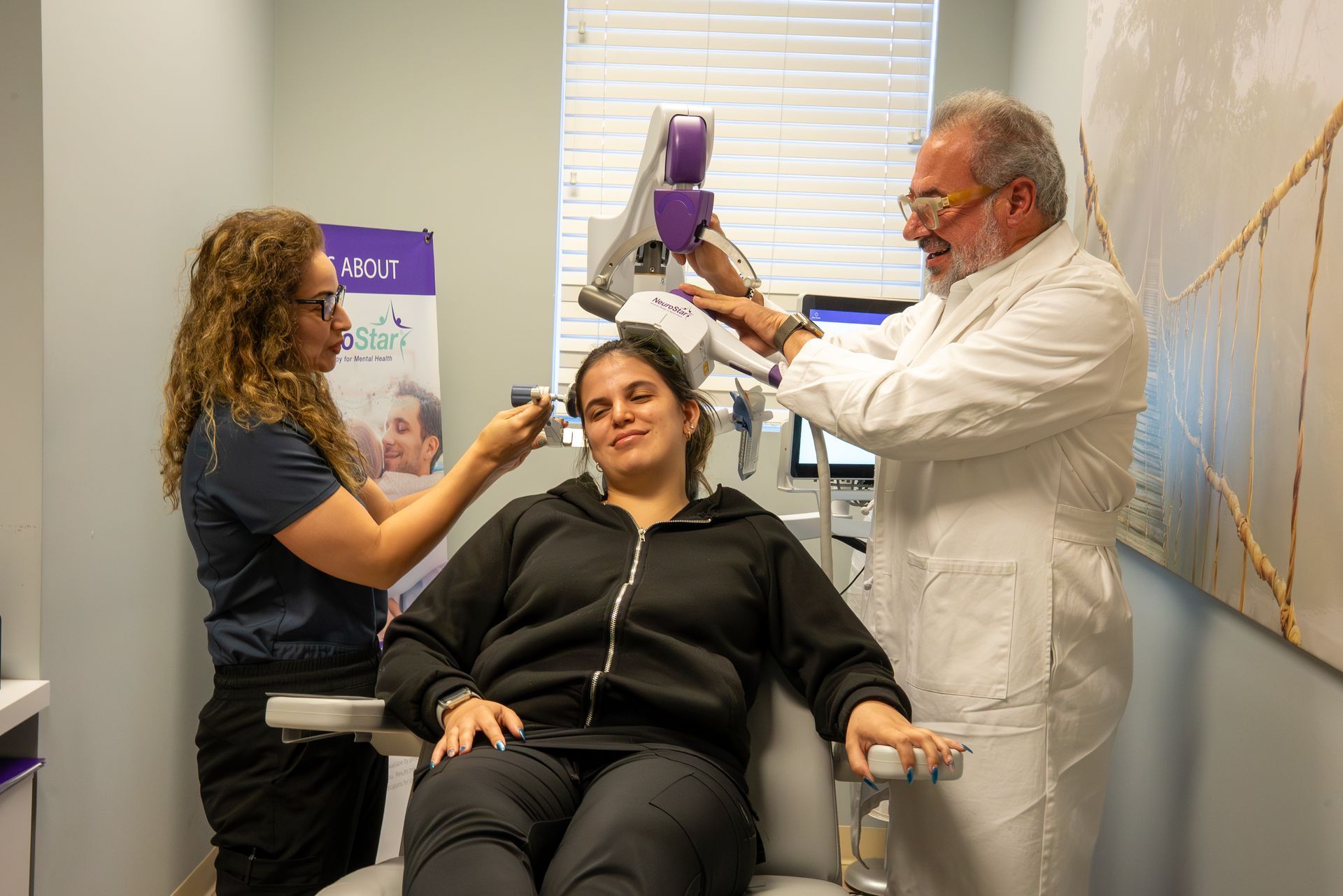Two clinicians adjust a purple device near a seated patient in a medical clinic room