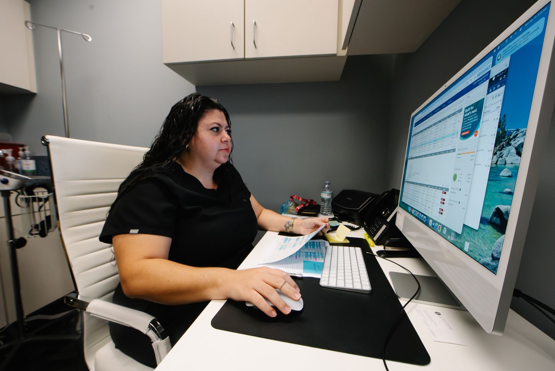 Person working at a desk with a large monitor in a small office, using a mouse and keyboard.