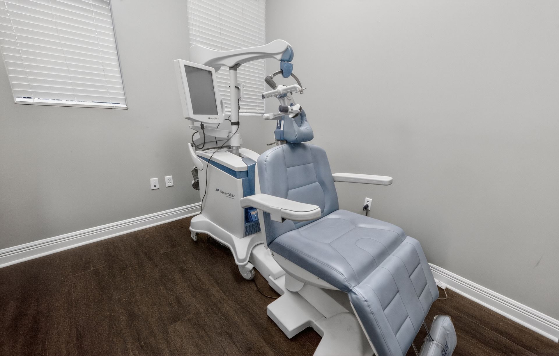 Dental chair and equipment in a small exam room with white walls and wood flooring