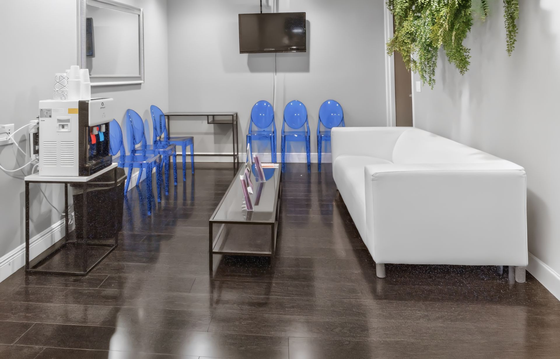 Empty modern waiting room with blue chairs, white sofa, and a glass coffee table on dark flooring