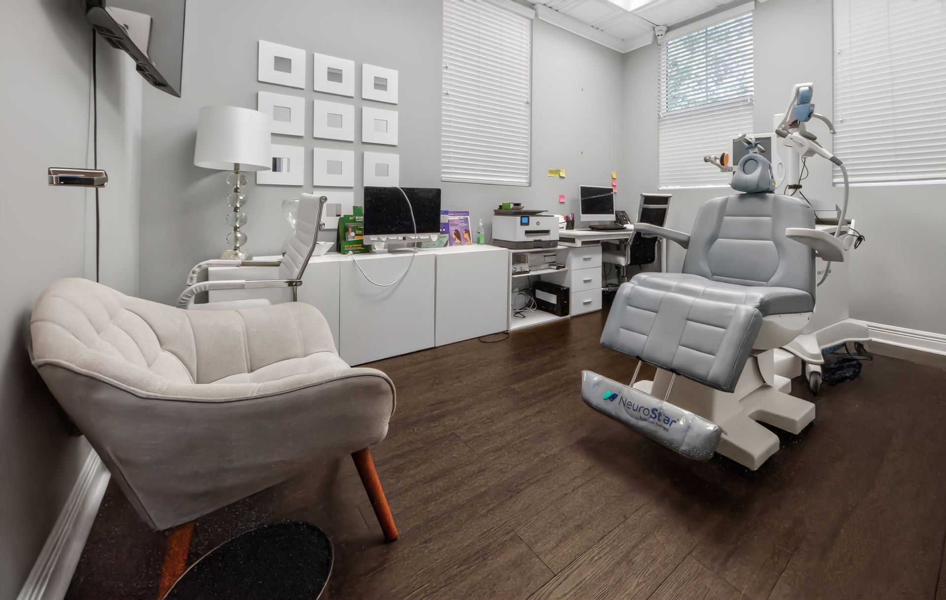Modern dental clinic with gray exam chair, beige guest chair, and treatment equipment on dark wood floor