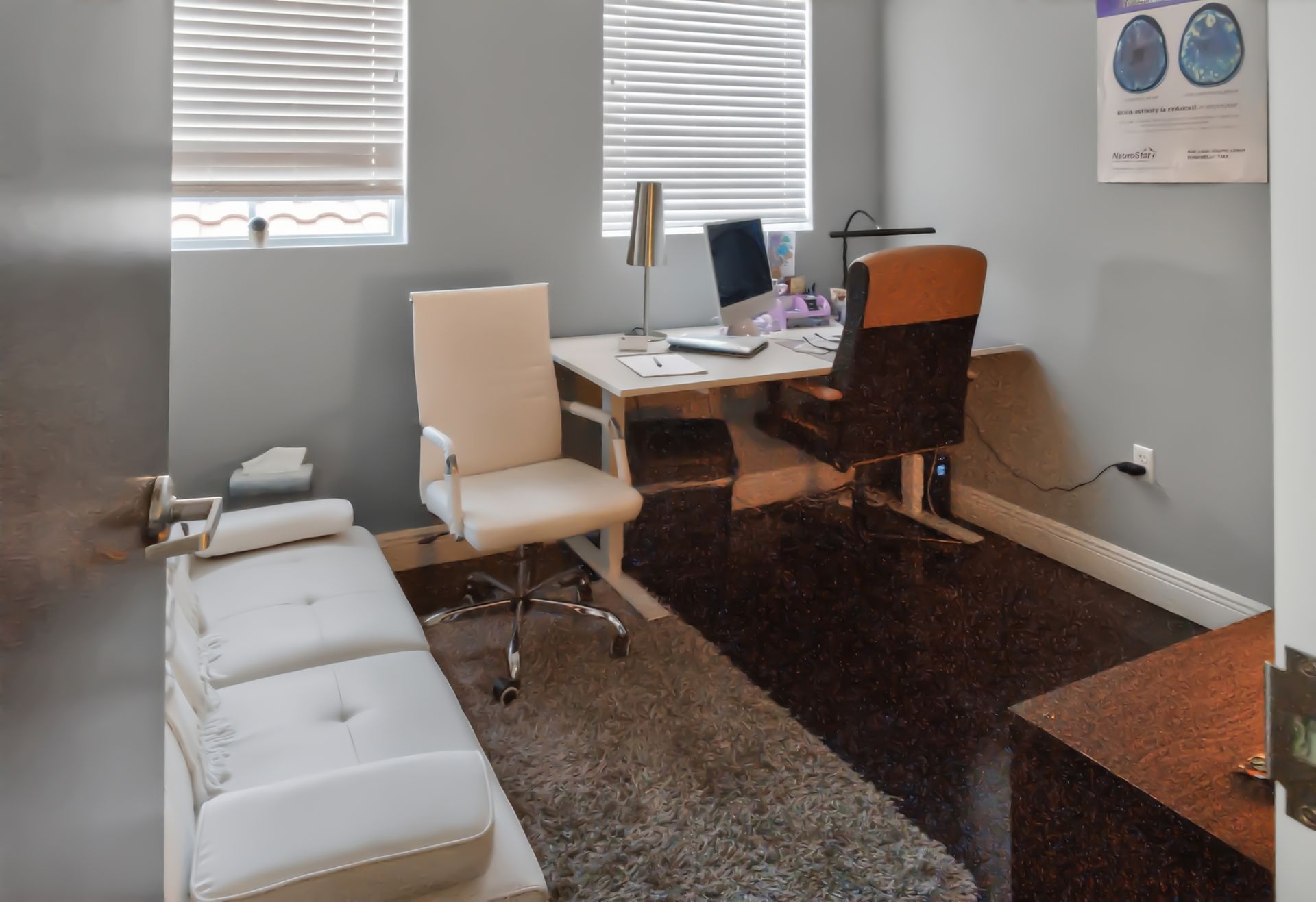 Small office with desk, computer, two chairs, sofa, and wall posters by windows with blinds