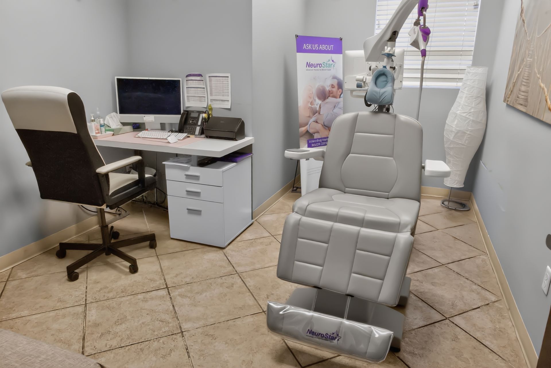 Exam room with padded dental chair, desk, computer, and medical equipment in a clinic setting