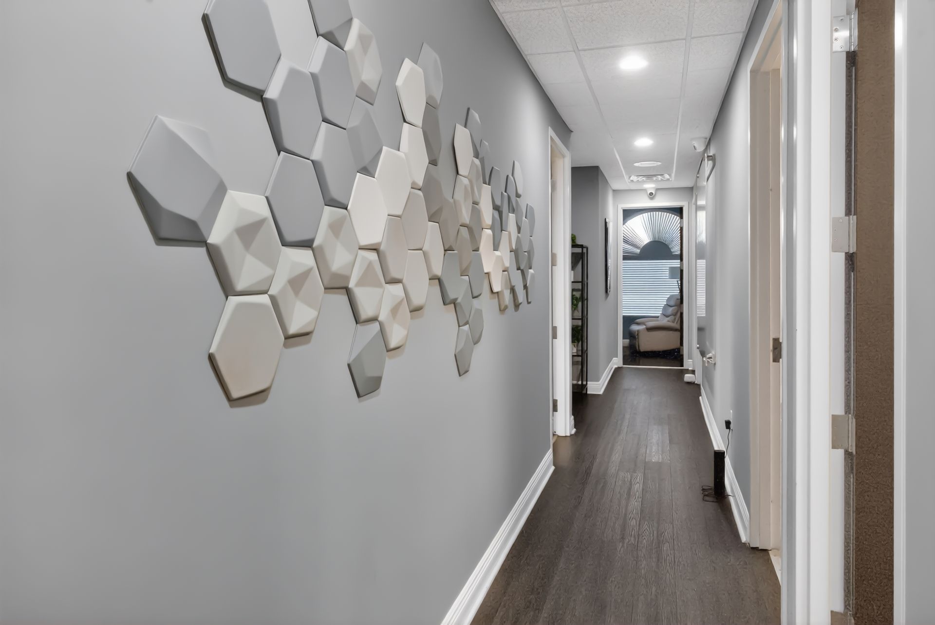 Long hallway with gray walls, dark wood floor, and hexagonal wall art on the left.
