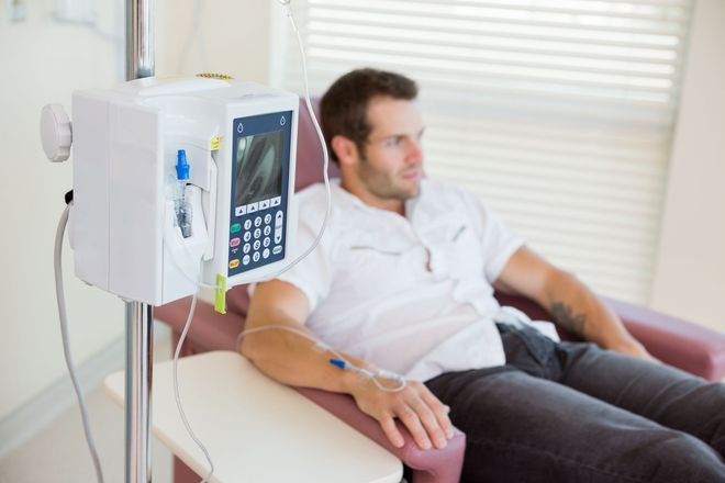 Patient reclining in a medical chair beside an infusion pump in a bright clinic room