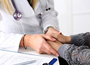 Doctor holding a patient's hands during a medical consultation on a white desk