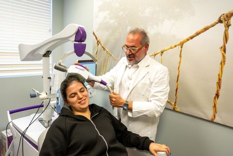 Dentist adjusting a dental scanner beside a reclining patient in a bright clinic